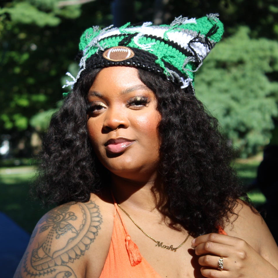 A woman outdoors in a park wearing a bright orange halter top and a green, white, and black patterned headband, with a tattoo visible on her upper arm.