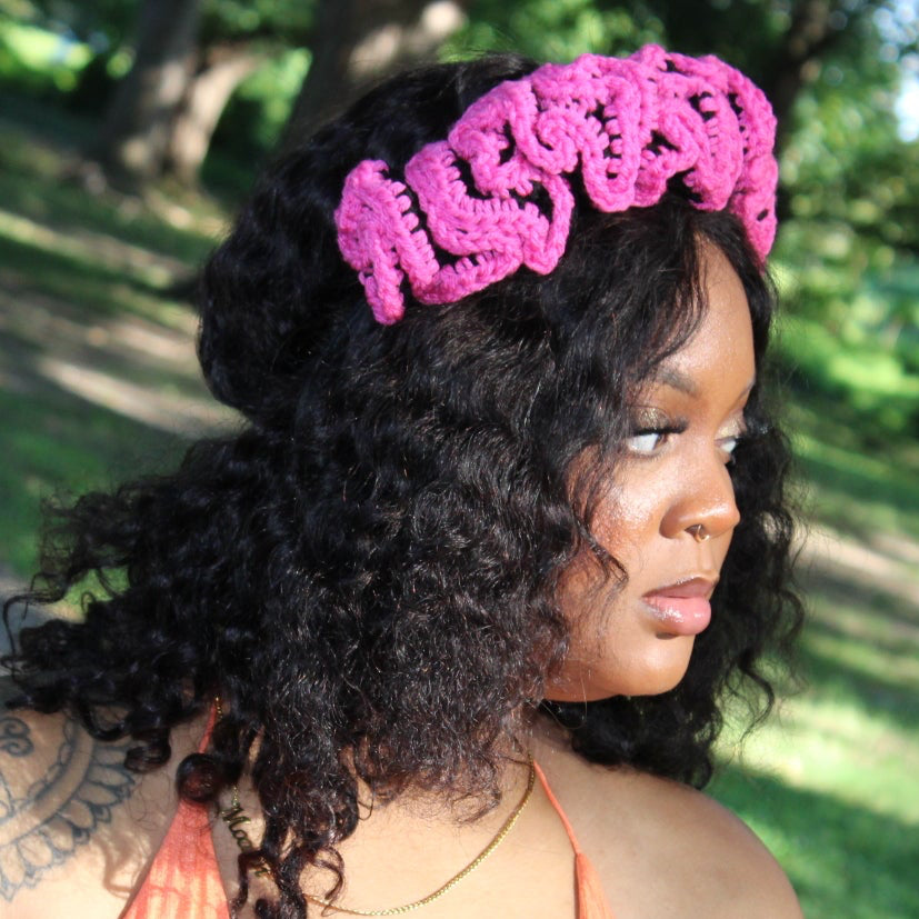 A woman outdoors wearing a bright pink crocheted headband with the word 'ALSOON' and a peach halter top, photographed in a park setting.